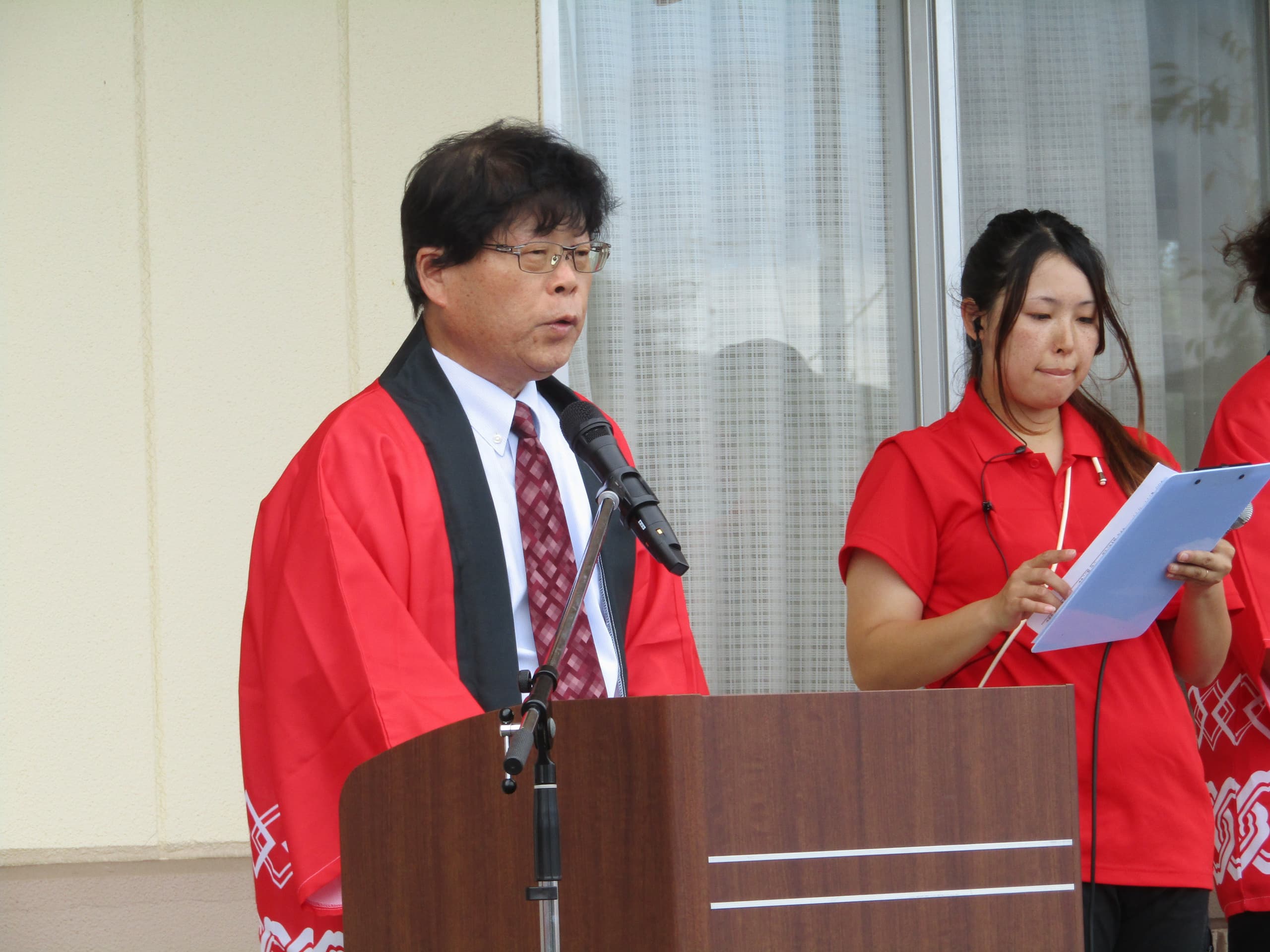 施設スタッフによるイベント・行事の進行風景。赤いユニフォーム姿で司会・進行中