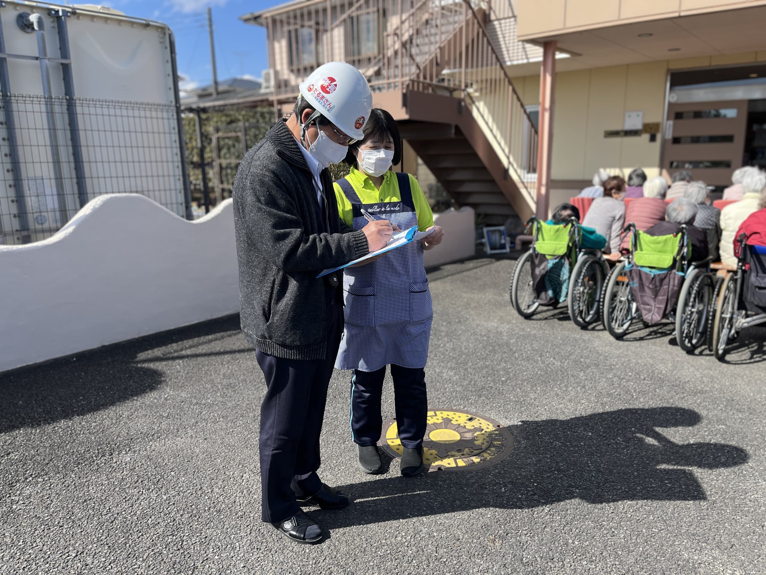 施設の外構で入居者と職員が交流する様子。安全管理の説明や指導の場面。